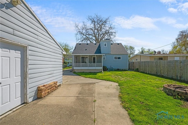 back of house featuring a patio, an outdoor fire pit, fence, a yard, and a sunroom