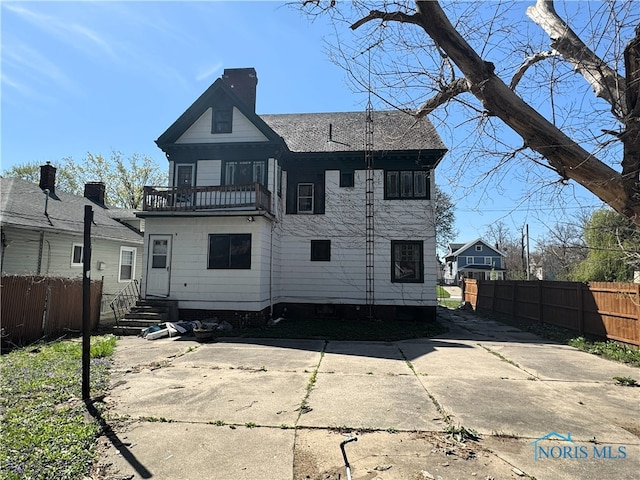 rear view of house with fence, a chimney, entry steps, and a balcony