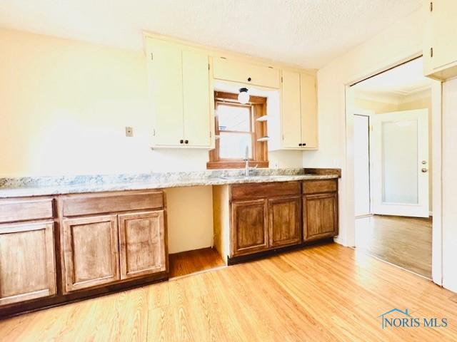 kitchen featuring light wood finished floors, a sink, light stone counters, and brown cabinetry