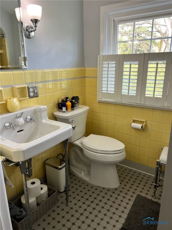 bathroom featuring tile walls, wainscoting, toilet, and a sink