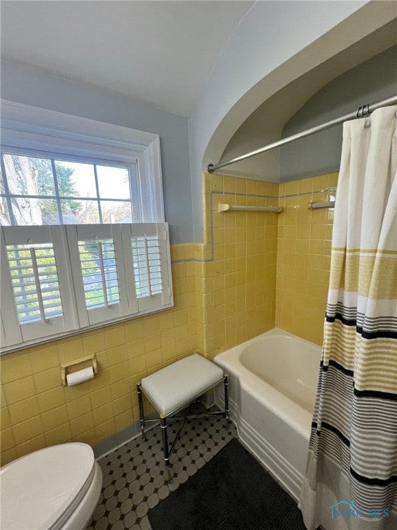 bathroom featuring shower / tub combo, toilet, tile walls, tile patterned floors, and wainscoting