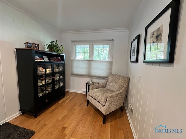 sitting room featuring light wood-style floors, crown molding, and a decorative wall