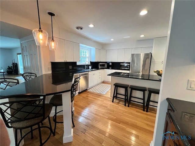 kitchen featuring a sink, stainless steel appliances, a kitchen bar, dark countertops, and white cabinets