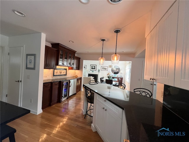 kitchen featuring light wood-style floors, glass insert cabinets, a kitchen breakfast bar, hanging light fixtures, and dark brown cabinets