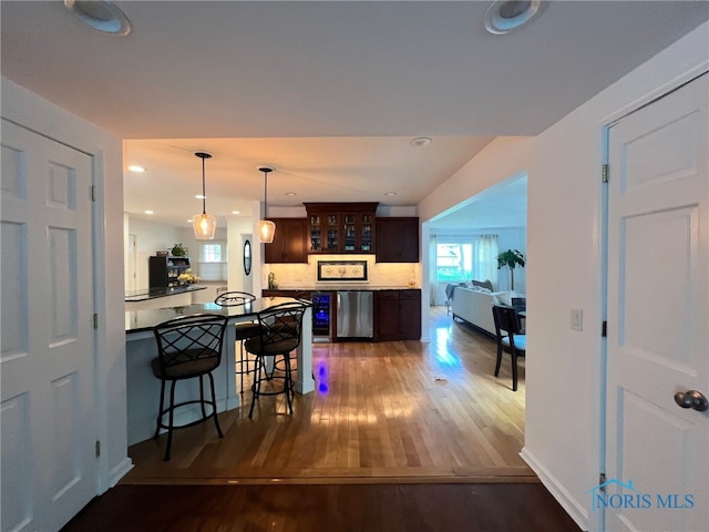 kitchen featuring glass insert cabinets, a breakfast bar, a peninsula, dark brown cabinets, and wood finished floors