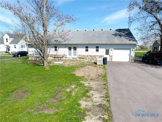 back of house featuring a yard, french doors, stone siding, and aphalt driveway