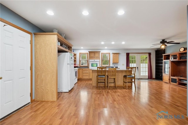 kitchen with recessed lighting, light wood finished floors, white appliances, and a kitchen bar