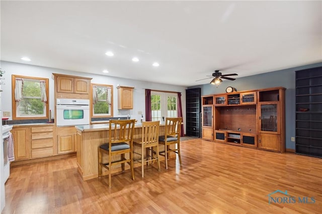 kitchen with light brown cabinetry, oven, light wood-style floors, a center island, and light countertops