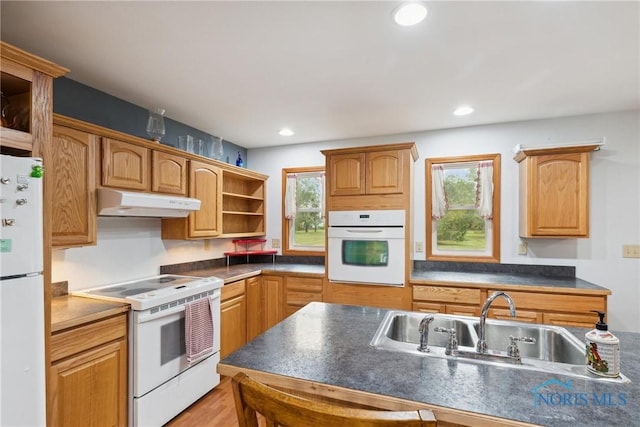 kitchen with dark countertops, open shelves, a sink, under cabinet range hood, and white appliances