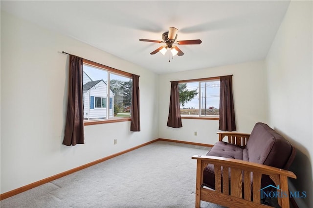 living area with a ceiling fan, baseboards, and light colored carpet