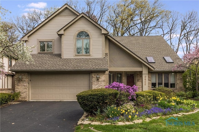 traditional home featuring roof with shingles, an attached garage, driveway, and brick siding