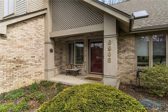 entrance to property featuring brick siding and roof with shingles