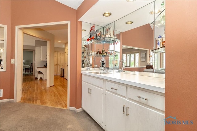 bar featuring baseboards, light carpet, and a sink