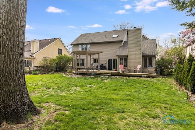 rear view of house with a shingled roof, a wooden deck, a chimney, and a yard
