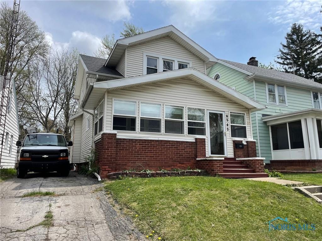 view of front of home featuring brick siding, driveway, entry steps, and a front lawn