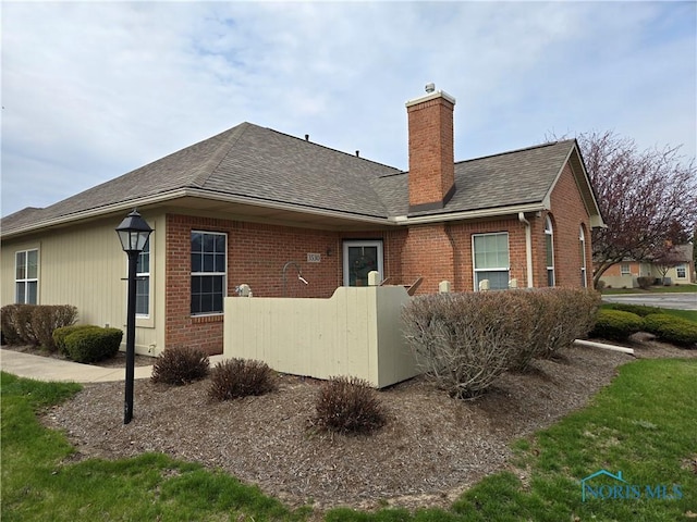 rear view of property with brick siding, a chimney, and a shingled roof