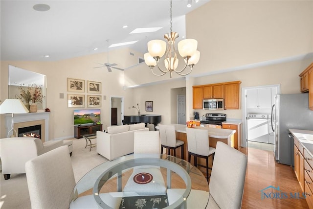 dining room featuring high vaulted ceiling, a glass covered fireplace, ceiling fan with notable chandelier, and light wood-type flooring