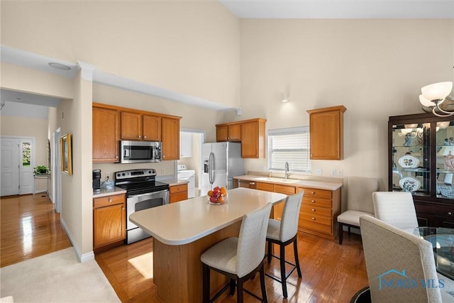 kitchen featuring a high ceiling, a center island, light countertops, a sink, and stainless steel appliances