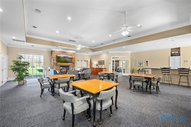 carpeted dining area with a ceiling fan, a tray ceiling, ornamental molding, and a fireplace