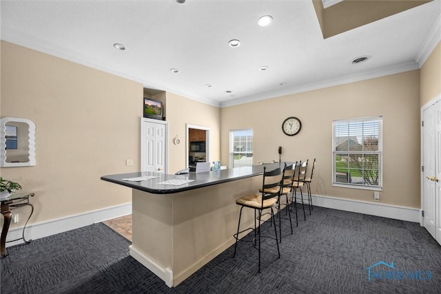 kitchen with dark carpet, ornamental molding, a breakfast bar area, and dark countertops