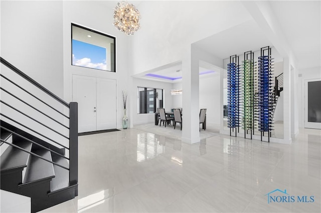 entryway featuring an inviting chandelier, tile patterned floors, baseboards, a towering ceiling, and stairway