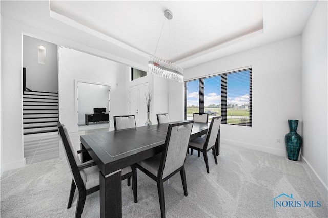 carpeted dining area with baseboards, a raised ceiling, and stairs