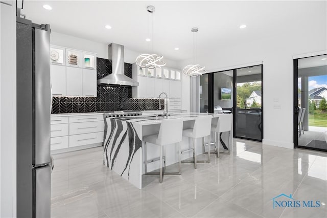 kitchen featuring wall chimney range hood, a kitchen breakfast bar, tasteful backsplash, a sink, and white cabinets