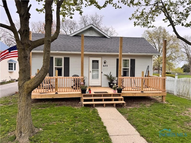 bungalow-style home with roof with shingles, fence, a wooden deck, and a front yard