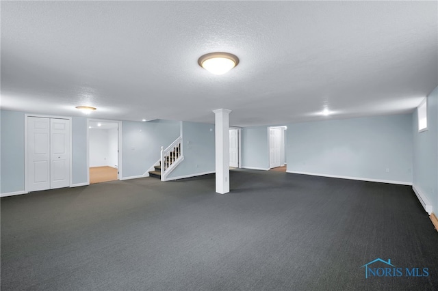 finished basement with a textured ceiling, baseboards, stairs, and dark carpet