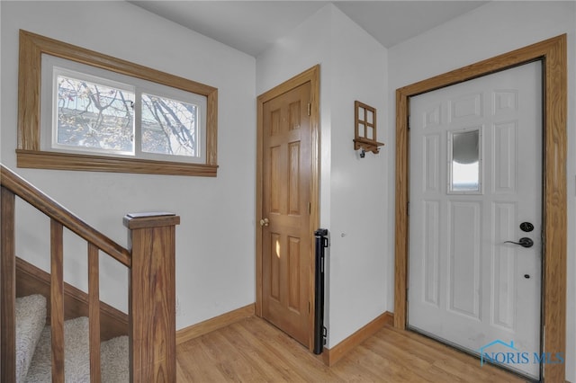 foyer entrance featuring baseboards, light wood-style flooring, and stairway