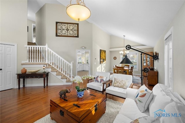 living room with wood finished floors, high vaulted ceiling, baseboards, an inviting chandelier, and stairs