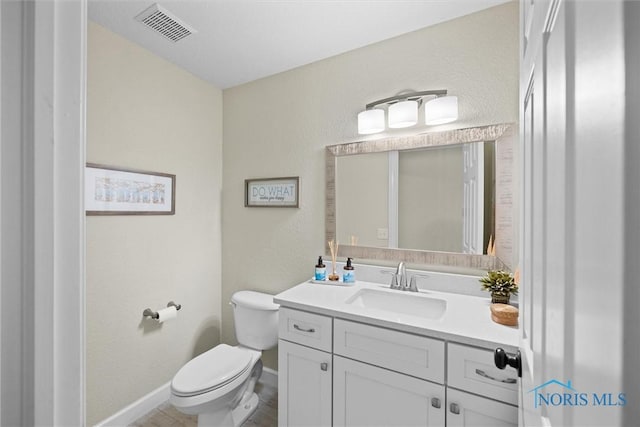 half bath featuring visible vents, baseboards, vanity, toilet, and a textured wall
