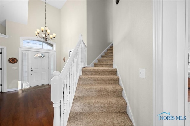 foyer entrance with a towering ceiling, baseboards, a chandelier, stairs, and dark wood-type flooring