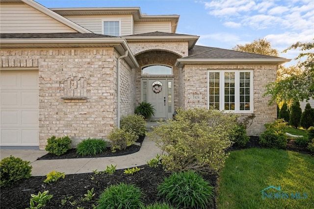 entrance to property featuring roof with shingles, an attached garage, and stone siding