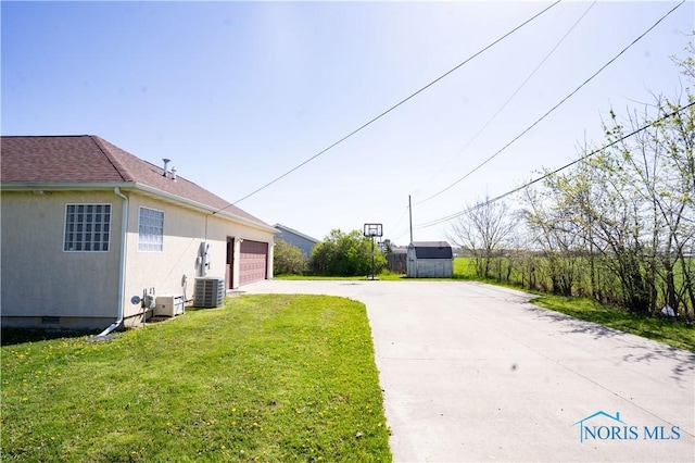 view of yard featuring concrete driveway, central AC, and a garage