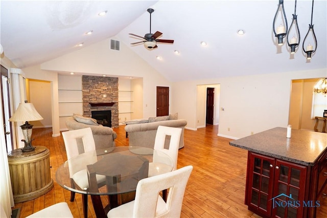 dining room featuring visible vents, a fireplace, light wood-type flooring, baseboards, and ceiling fan with notable chandelier