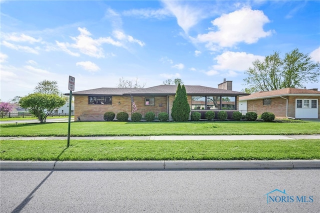 ranch-style house with a chimney, brick siding, and a front yard