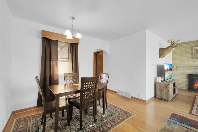dining space with a notable chandelier, arched walkways, baseboards, light wood-type flooring, and visible vents