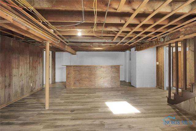 finished below grade area featuring wood finished floors, wooden walls, and stairway