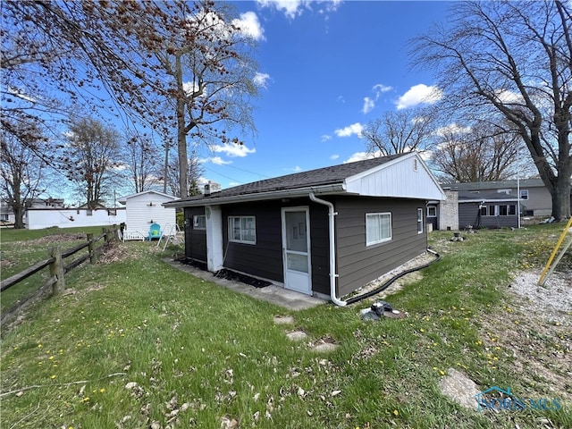 rear view of property with a lawn, fence, and an outbuilding