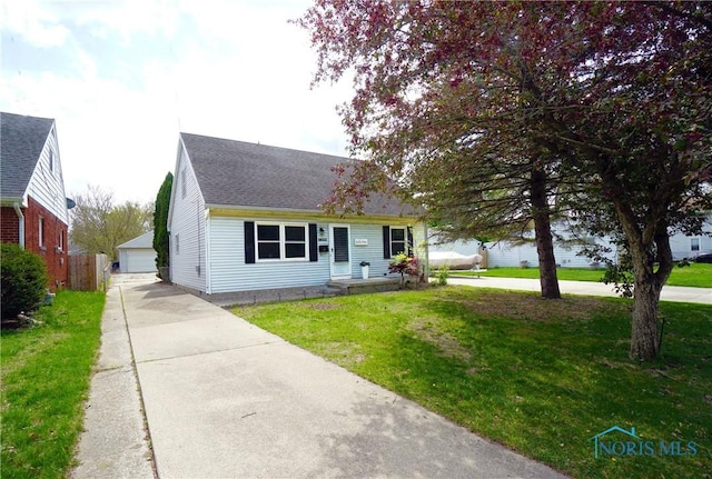 cape cod home featuring a detached garage, roof with shingles, an outbuilding, and a front yard