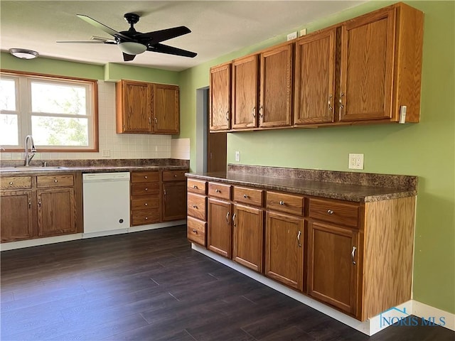 kitchen with white dishwasher, dark countertops, a sink, brown cabinetry, and dark wood-style floors