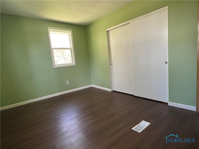 unfurnished bedroom with visible vents, a closet, baseboards, dark wood-type flooring, and a textured ceiling
