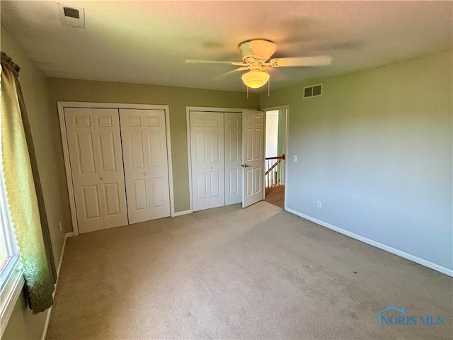 unfurnished bedroom with carpet floors, multiple closets, visible vents, and baseboards
