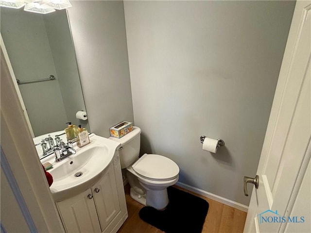 half bathroom with vanity, baseboards, wood finished floors, and toilet