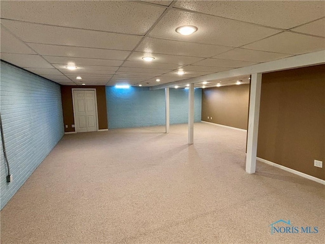 finished basement with carpet flooring, brick wall, a drop ceiling, and baseboards