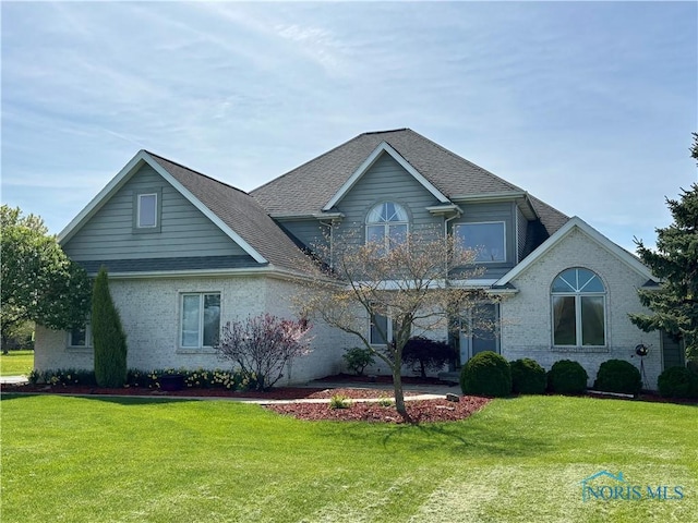 view of front of house with a shingled roof, a front lawn, and brick siding