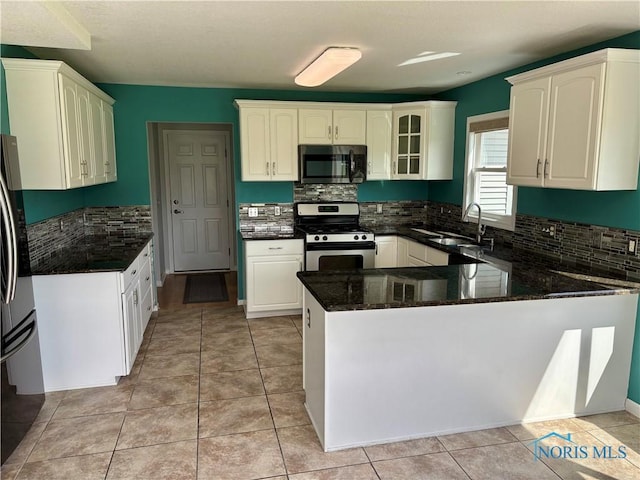 kitchen featuring backsplash, appliances with stainless steel finishes, a sink, dark stone countertops, and a peninsula