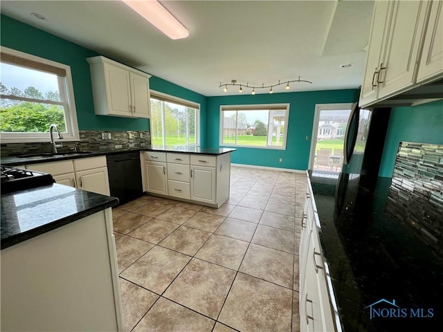 kitchen featuring a peninsula, dark countertops, black dishwasher, a sink, and a wealth of natural light