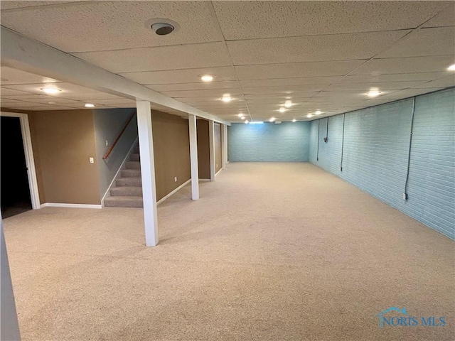 finished below grade area featuring stairs, carpet, and a drop ceiling